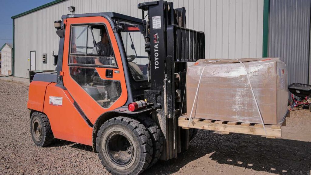 An orange forklift with a cardboard wrapped pallet on the forks.