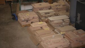 Various sets of cabinet doors (some MDF, some wood) laid out on pallets in a factory.