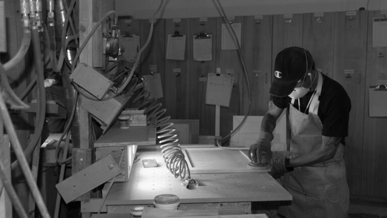 A black-and-white picture of an employee sanding a cabinet door at their workstation. Warranty cabinet doors can cause frustration, so save time by ordering them online.