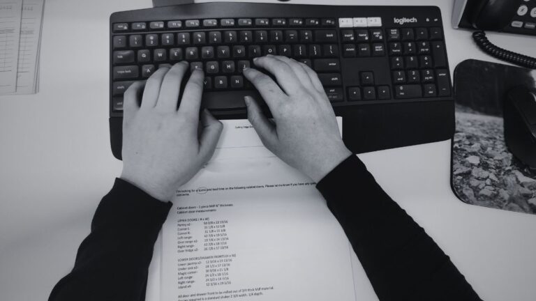 A black and white image of hands on a computer keyboard.