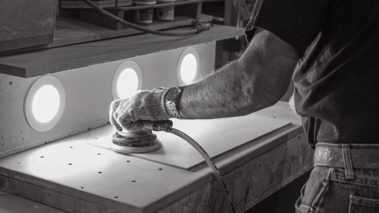 A black and white image of a worker sanding a thin piece of MDF.