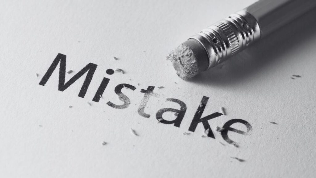 A black and white image of the word Mistake, partially erased, with a pencil lying in the top right corner.