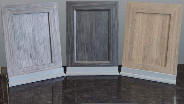 Three NEXGEN cabinet doors (one grey, one dark grey, and one brown) on a black countertop.