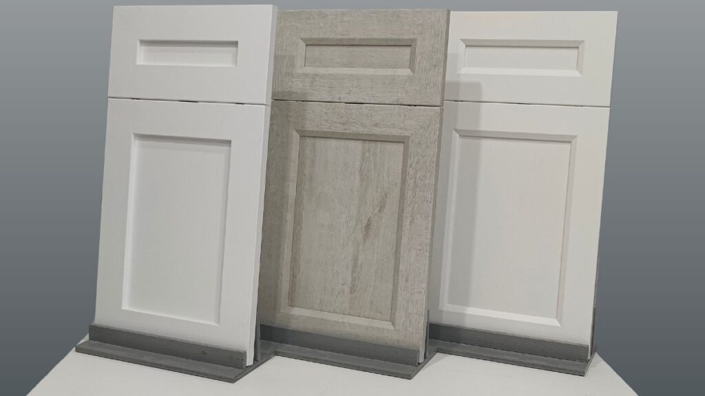 Three NEXGEN cabinet doors. From left to right, a white cabinet door, a light grey woodgrain cabinet door, and a cream cabinet door.