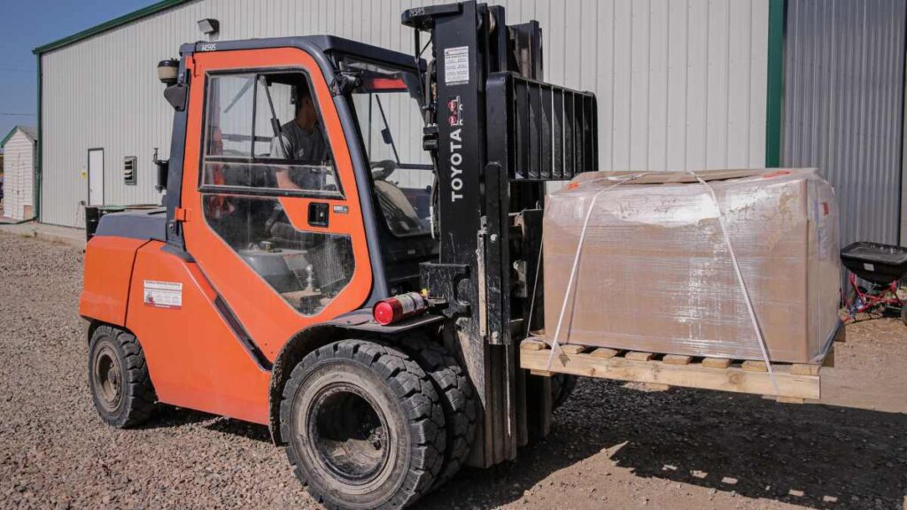 An orange forklift with a cardboard-wrapped skid of cabinet doors on the forks.