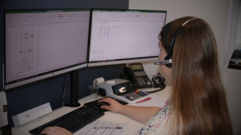 A woman sitting at a desk with two computer screens.