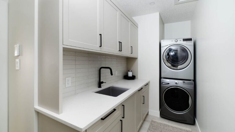 A laundry room with cream painted 1 piece MDF cabinet doors, black handles, and a dark grey washer and dryer.