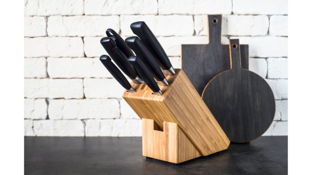 A wooden knife block on a black countertop, with two black cutting boards in the background.