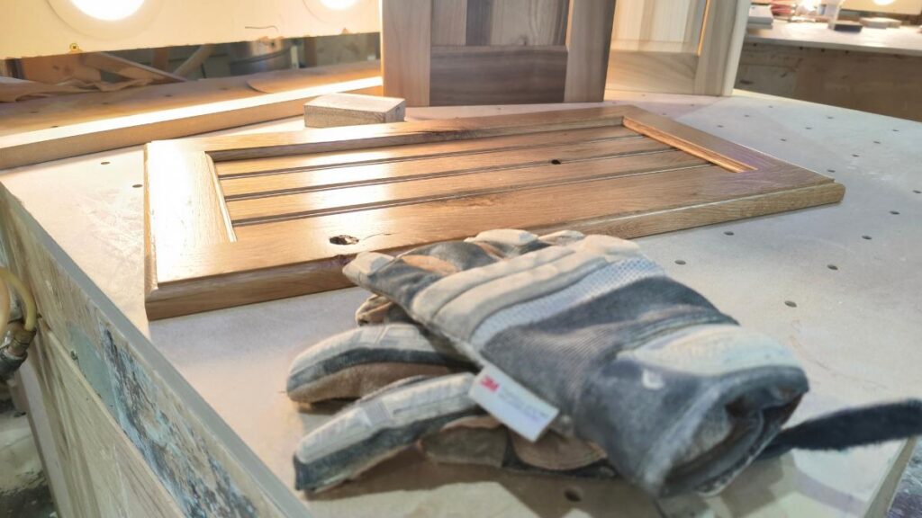 A pair of gloves lying on a pegboard table, with three cope and stick cabinet doors in the background.