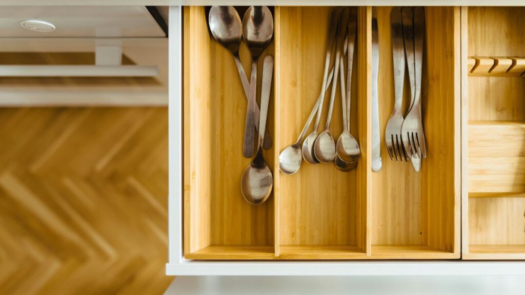 A bamboo drawer organizer containing silverware. In the background, a golden-brown chevron floor.