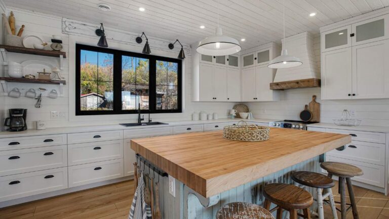 A kitchen with white finished cabinet doors, slat wall paneling, and a wood butcher block countertop.