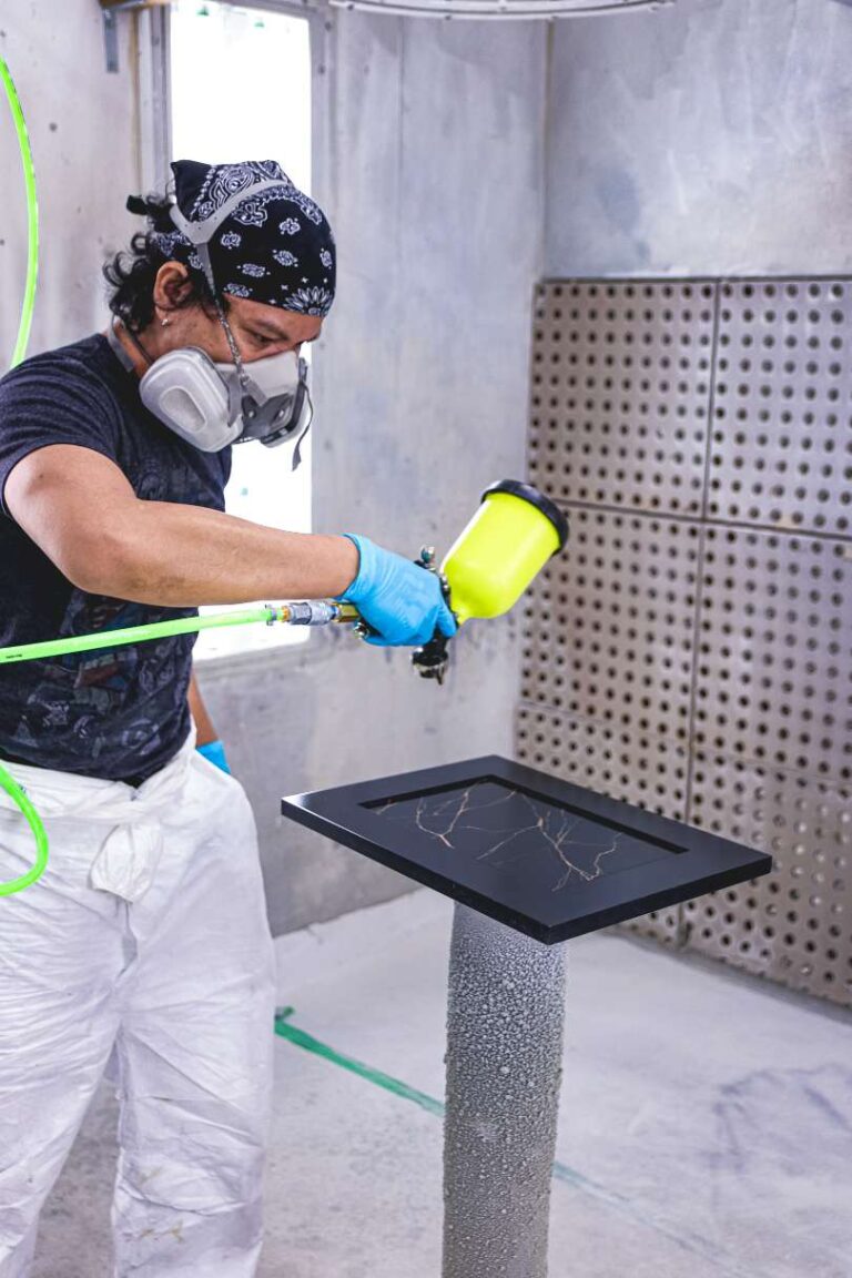 An employee spraying a black finished cabinet door with gold marbling on the panel.