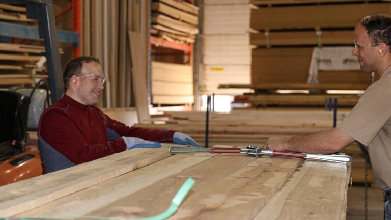 Cutting Edge stocks raw lumber for its cabinet doors. In this image, two employees are standing next to a lift of lumber.