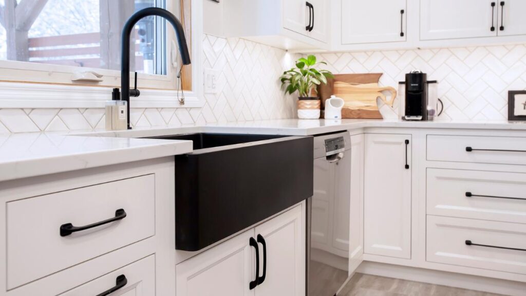 A kitchen with white painted cabinet doors, black handles, and a black farmhouse sink.