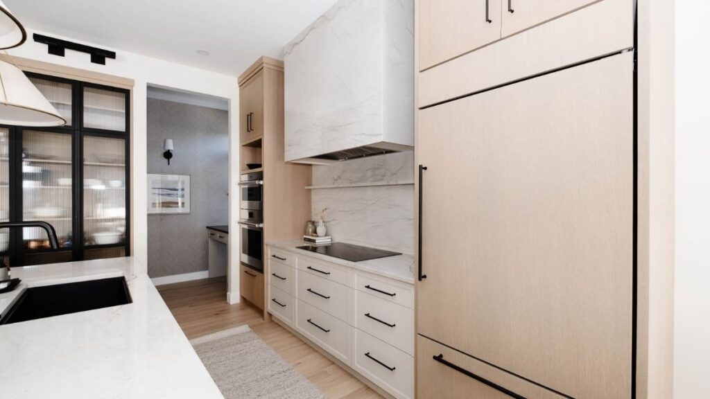 A kitchen with whitewashed Rift Cut White Oak cabinet doors and white painted cabinet doors, black accents, and white marble countertops and backsplash.