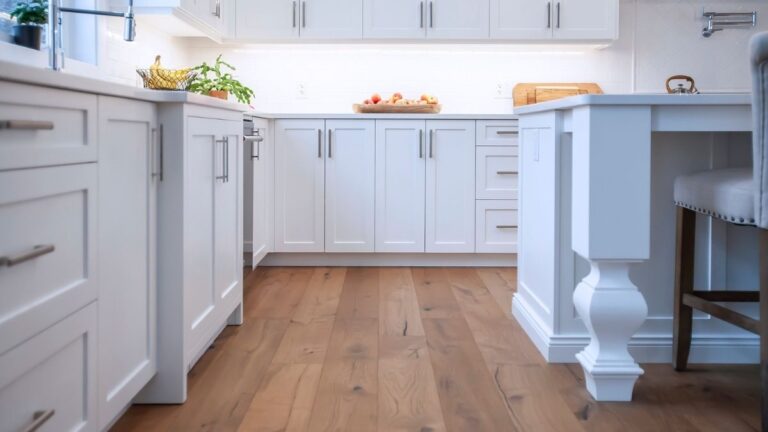 A kitchen with white painted MDF cabinet doors, brown wood-patterned flooring, and silver hardware.