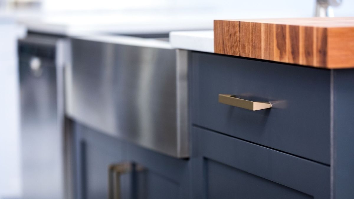 A kitchen island with blue painted cabinet doors, a stainless steel farmhouse sink, and a built-in butcher block board. Finished cabinet doors take longer to make than raw cabinet doors.