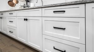 A bank of cabinets with white painted cabinet doors and drawer fronts and black hardware. Caliber Cabinet Solutions works with homeowners in Moose Jaw.