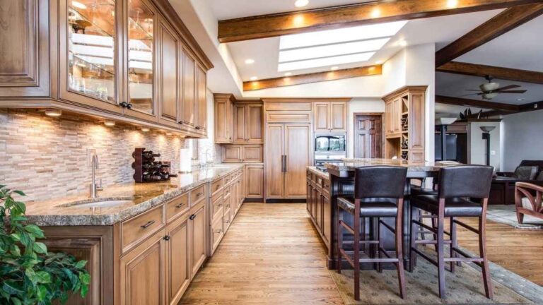 A kitchen with light-brown cabinet doors, brown tile backsplash and a quartz countertop. It requires skill to get consistent colour with a spray stain finish.