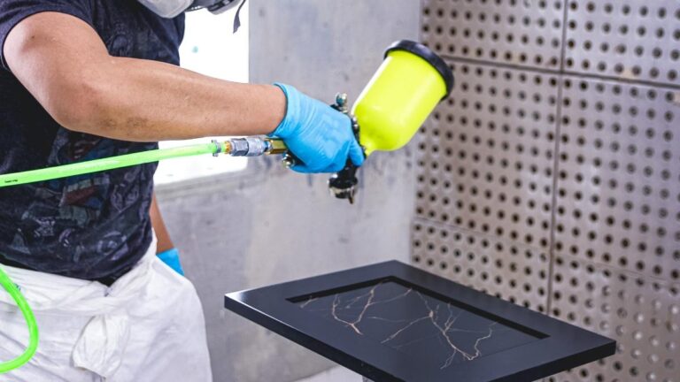 An employee spraying a painted cabinet door. You can reduce the amount of colour inconsistency with a spray stain finish by maintaining a consistent distance from the door.