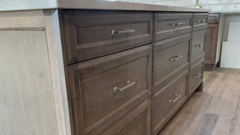 An island with grey-stained Maple cabinet doors and silver hardware.