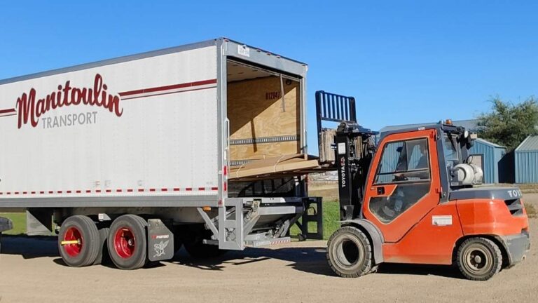 An orange forklift loading a pallet into a white and red trailer with the Manitoulin logo on the side. Cutting Edge ships cabinet doors to Regina via Manitoulin Transport.