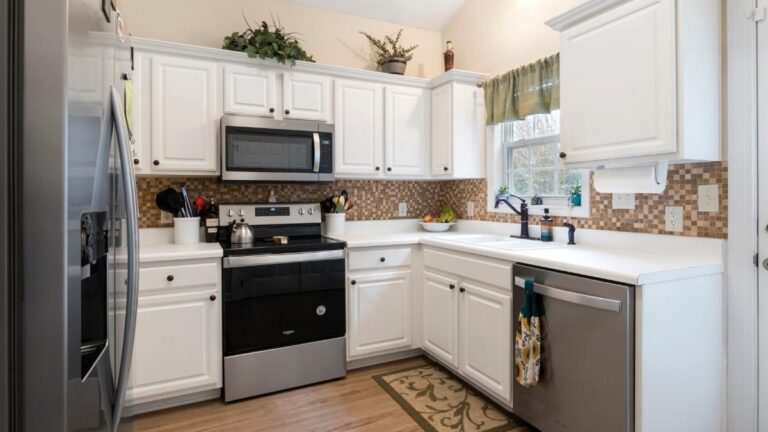 A kitchen with white thermofoil cabinet doors, brown tile backsplash and stainless steel appliances.